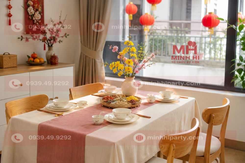 Trang trí Tết 2027 cho nhà bếp với bàn ăn phủ khăn kem, bình hoa thấp, bộ chén đĩa và khay mứt Tết.