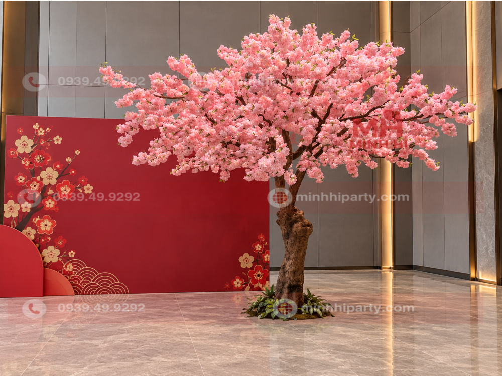 Cây đào giả trang trí sự kiện Tết 2027 có tán hoa hồng lớn, đặt bên phải backdrop đỏ ghi Xuân Đinh Mùi 2027.
