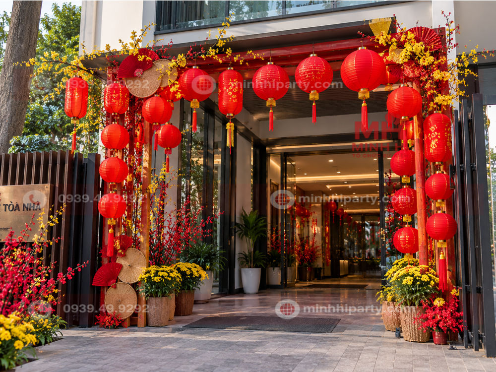 Đèn lồng đỏ trang trí cổng chào Tết tại lối vào tòa nhà hiện đại, kết hợp hoa mai vàng, hoa đào và các phụ kiện trang trí truyền thống.