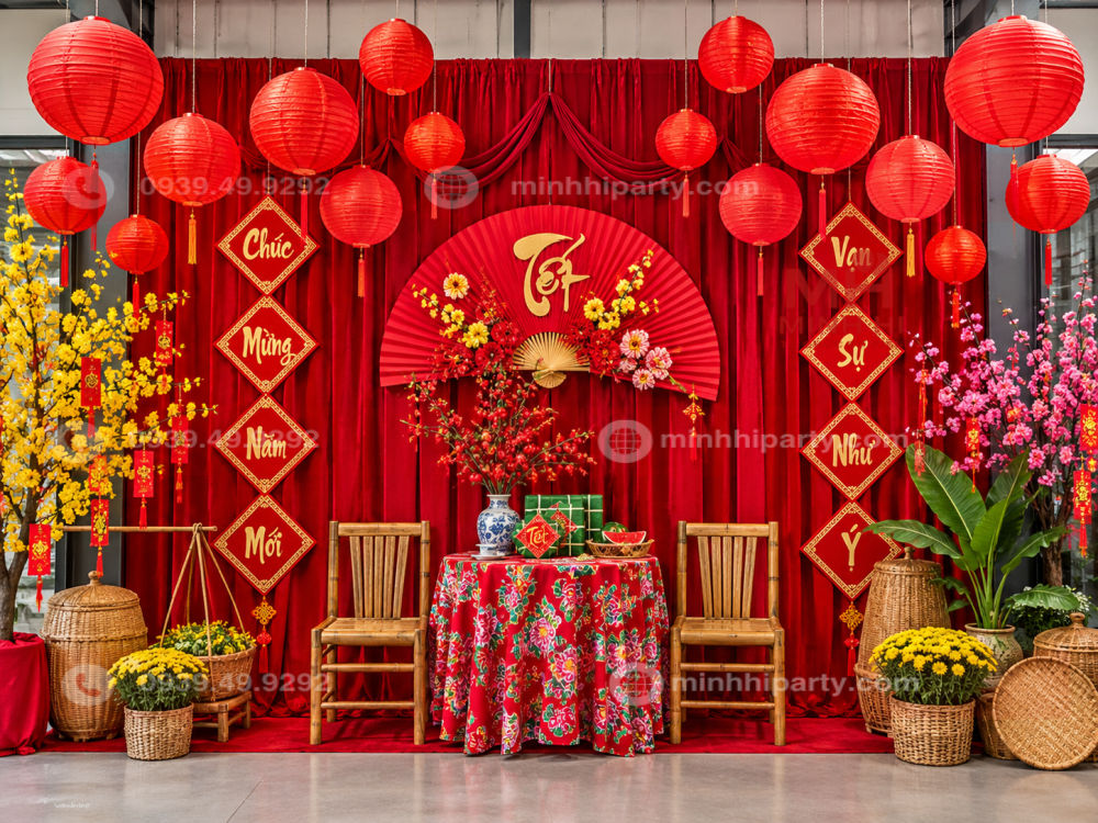 Đèn lồng trang trí tiểu cảnh Tết treo trước phông rèm đỏ, kết hợp hoa mai, hoa đào, bàn tre, quạt Tết và phụ kiện truyền thống.