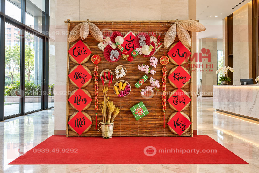 Tiểu cảnh Tết 2027 cho chung cư với phông mành tre, câu đối đỏ và mô hình bánh chưng trên thảm đỏ tại sảnh.